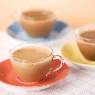 Foto: tres tazas de café con leche en platillos naranja, azul y amarillo sobre mantel cuadriculado