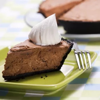 Photograph of a chocolate pie slice with whipped cream on a green plate and fork